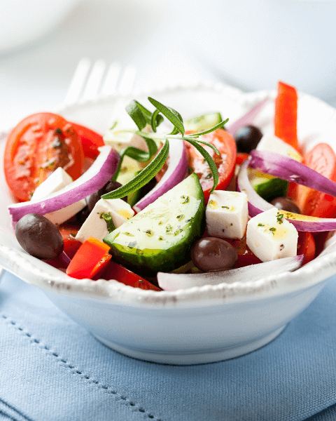 Bowl of Greek salad with cucumber, red onion, tomatoes, olive, and feta cheese.